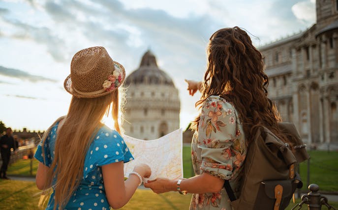 Two tourists with a map near the Leaning Tower of Pisa and Cathedral, Pisa, Italy.