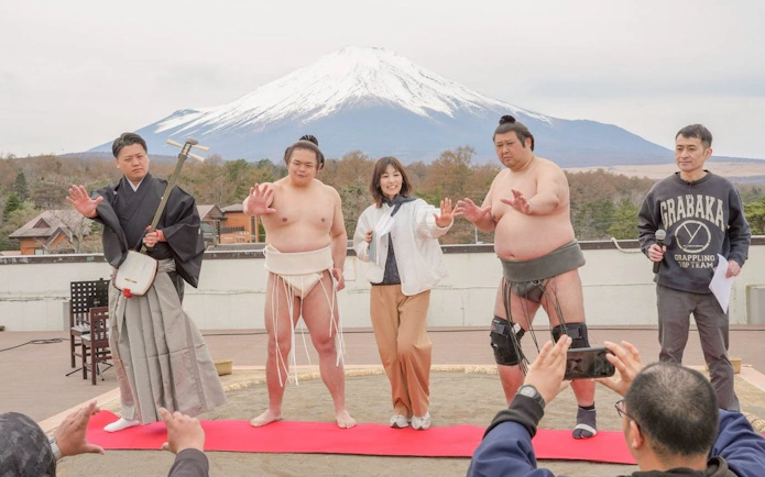 Sumo wrestlers and a guide pose with Mount Fuji in the background during a Yamanashi sumo show experience.