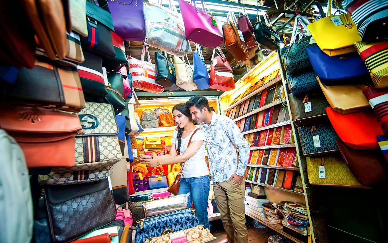 Couple shopping at a vibrant handbag stall in Kuala Lumpur local market.