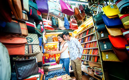 Couple shopping at a vibrant handbag stall in Kuala Lumpur local market.