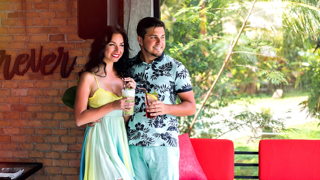 Un homme portant un t-shirt à fleurs et une femme portant une robe cintrée à l'intérieur d'une maison