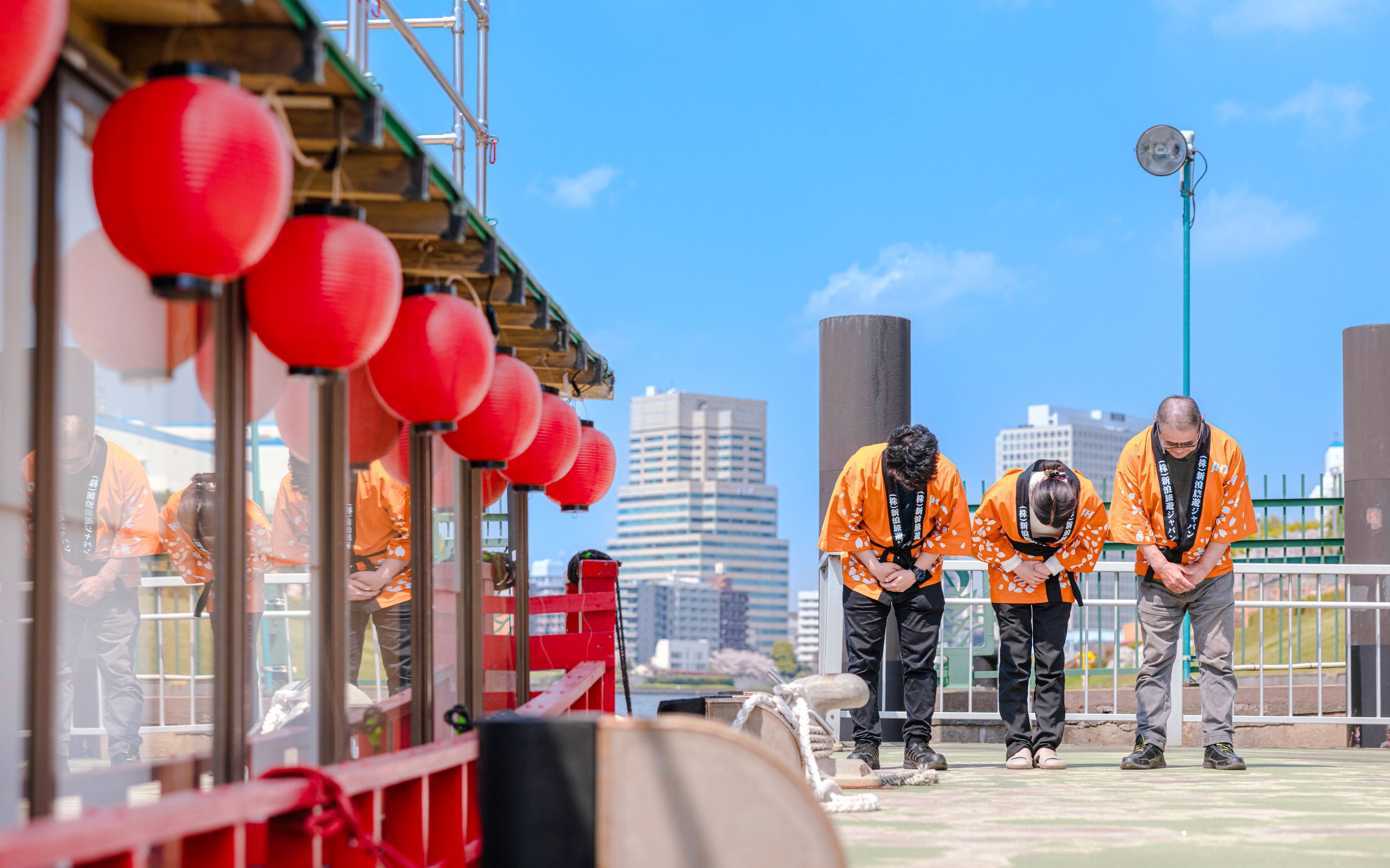 People bowing in traditional attire on a Tokyo rooftop with red lanterns during a spring tea ceremony.