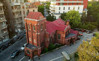 Red brick church in Bucharest surrounded by urban buildings, part of the self-guided city exploration game.