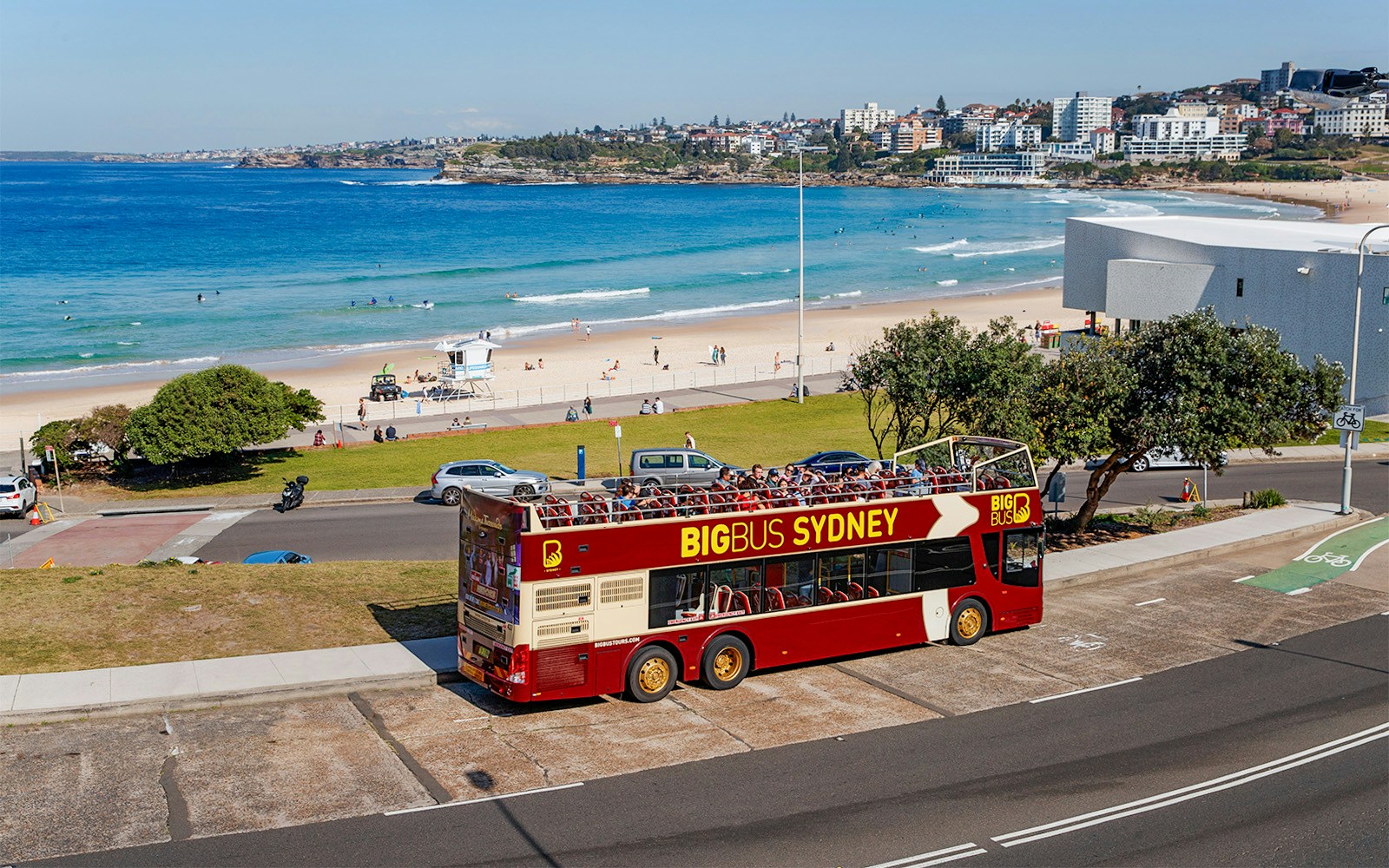 Big Bus Sydney parked near Bondi Beach with ocean and cityscape in the background.
