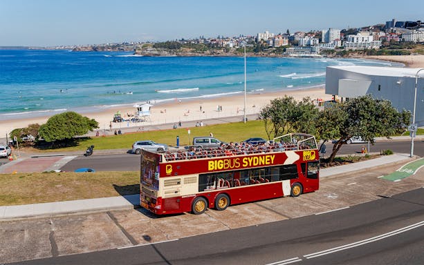 Big Bus Sydney parked near Bondi Beach with ocean and cityscape in the background.