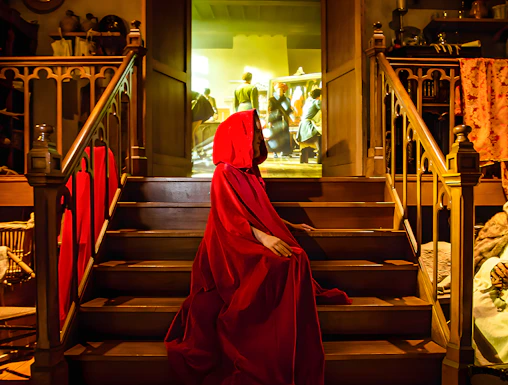 Person in red cloak on stairs at Bruges Historium exhibit.