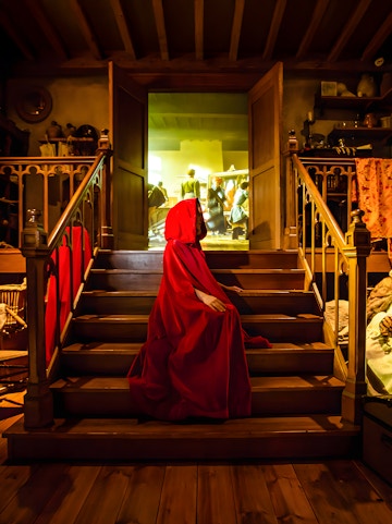 Person in red cloak on stairs at Bruges Historium exhibit.