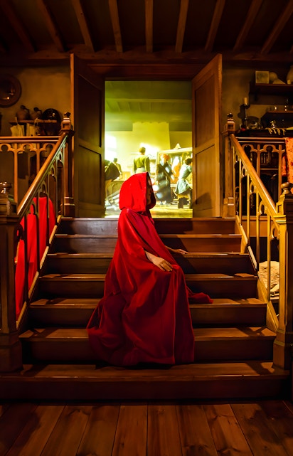 Person in red cloak on stairs at Bruges Historium exhibit.