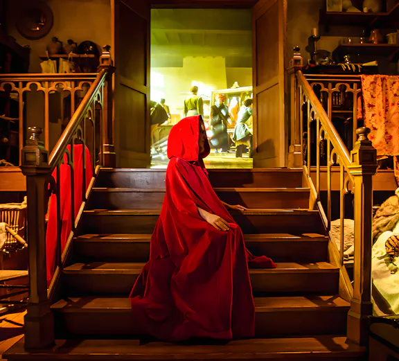 Person in red cloak on stairs at Bruges Historium exhibit.