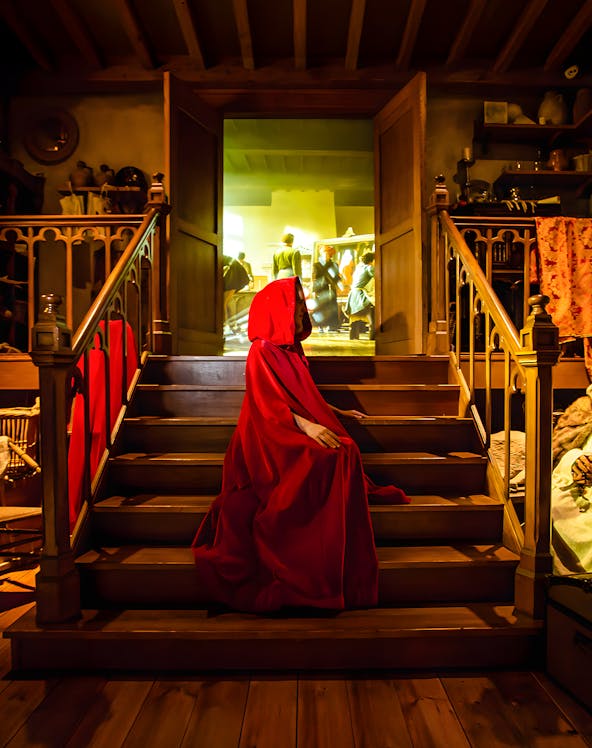 Person in red cloak on stairs at Bruges Historium exhibit.
