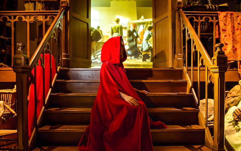 Person in red cloak on stairs at Bruges Historium exhibit.