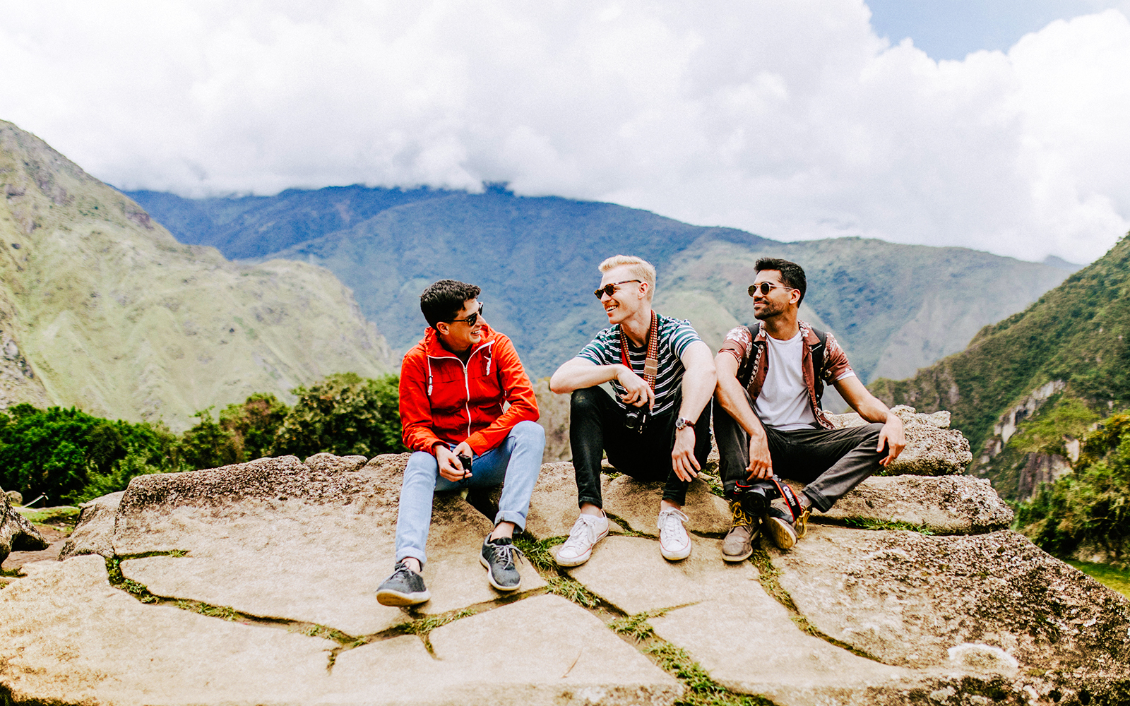 Tourists sitting on stone ledge with Machu Picchu mountains in background.