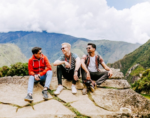 Tourists sitting on stone ledge with Machu Picchu mountains in background.