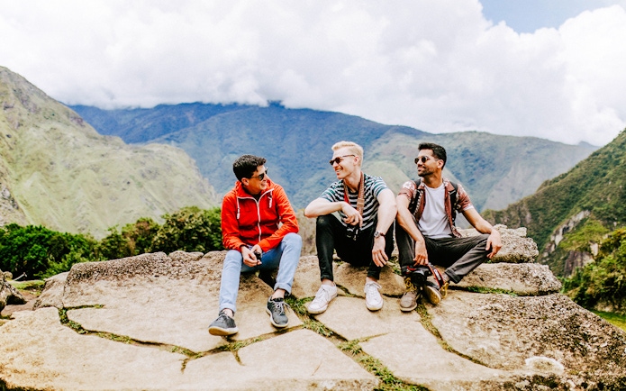 Tourists sitting on stone ledge with Machu Picchu mountains in background.