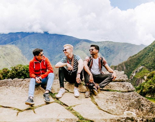 Tourists sitting on stone ledge with Machu Picchu mountains in background.