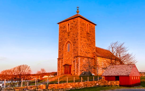 St. Olav's Church at Avaldsnes with stone tower and red wooden building.