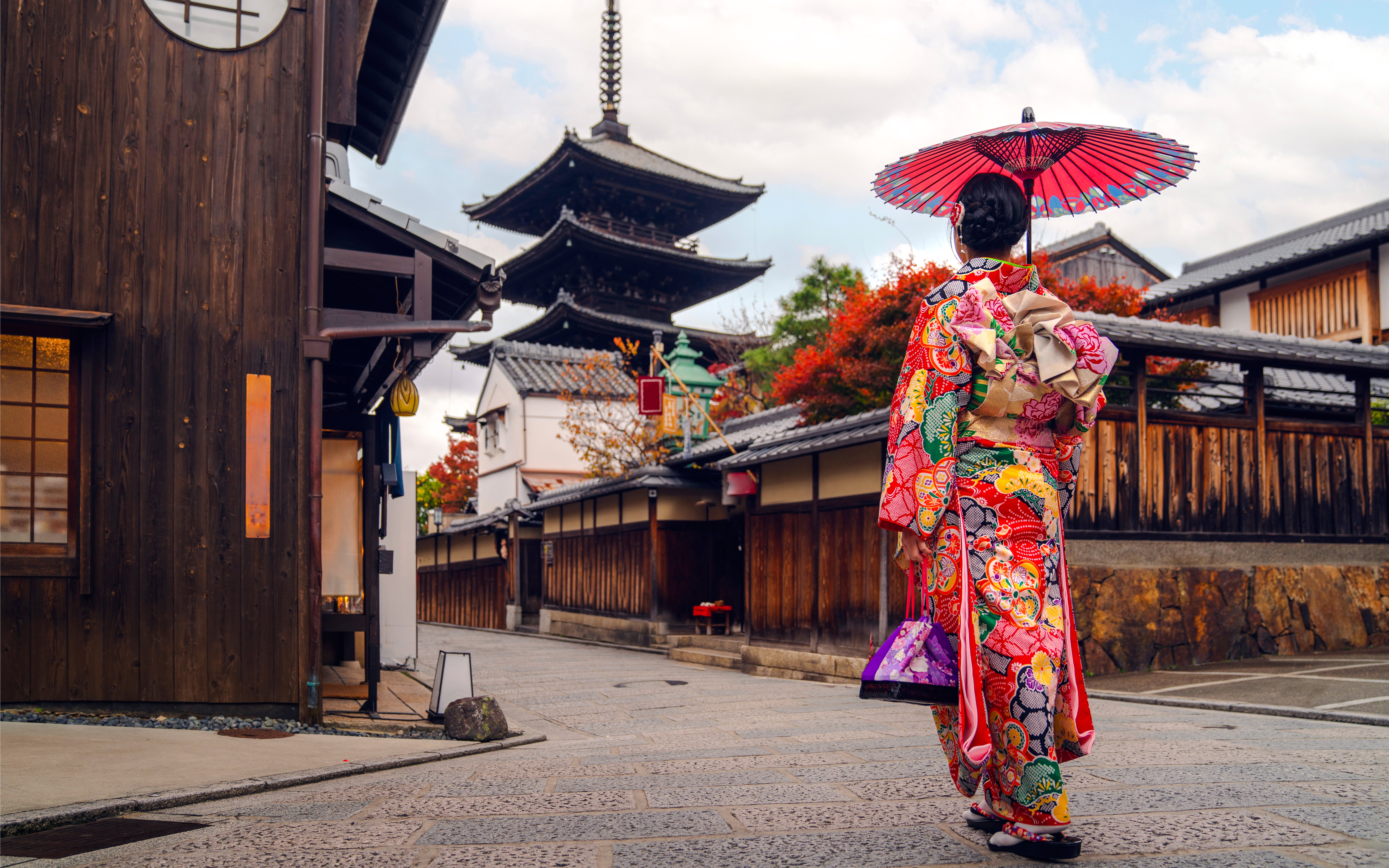 Asian woman in kimono walking near pagoda in Kyoto, Japan.