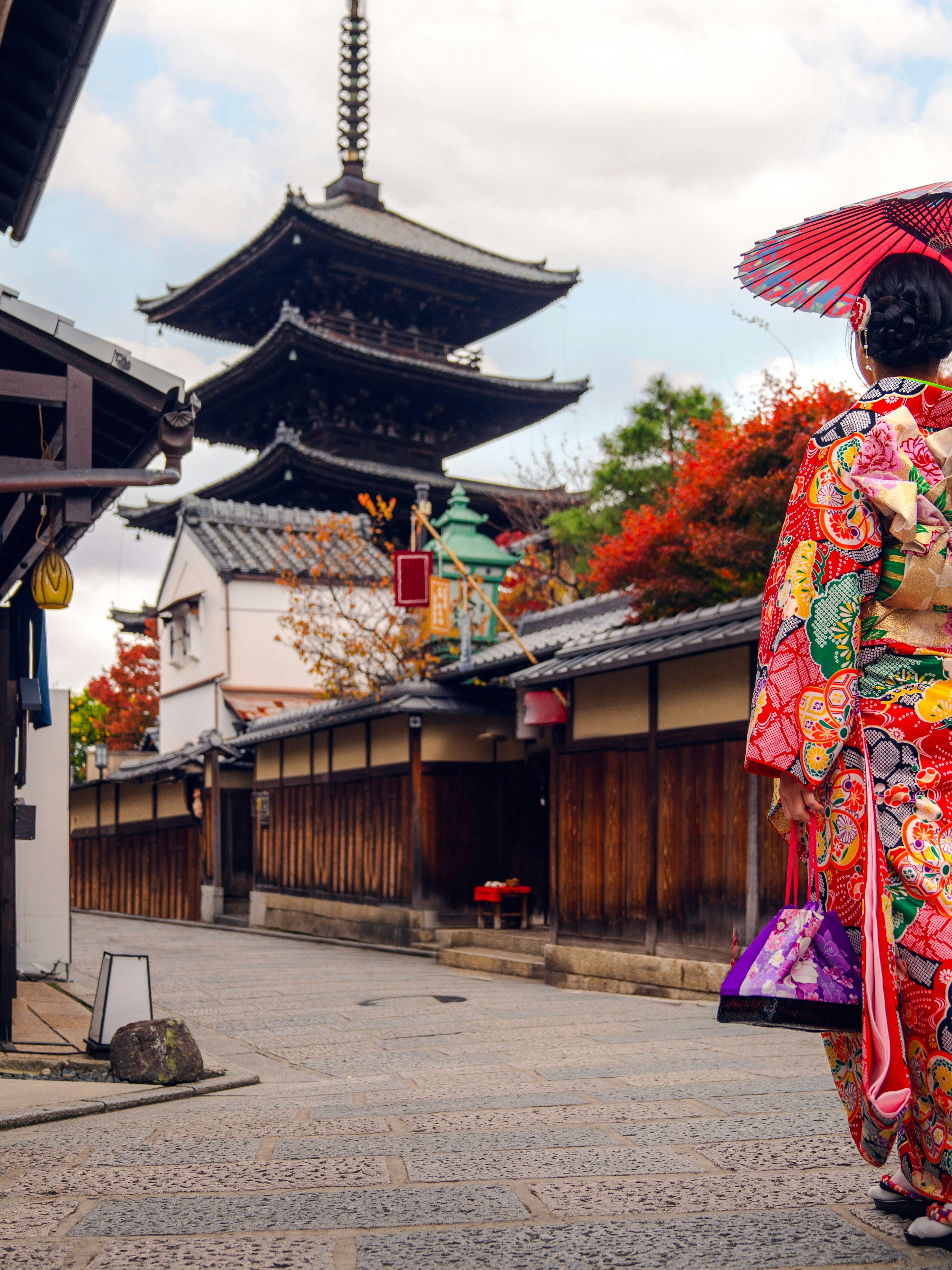 Asian woman in kimono walking near pagoda in Kyoto, Japan.