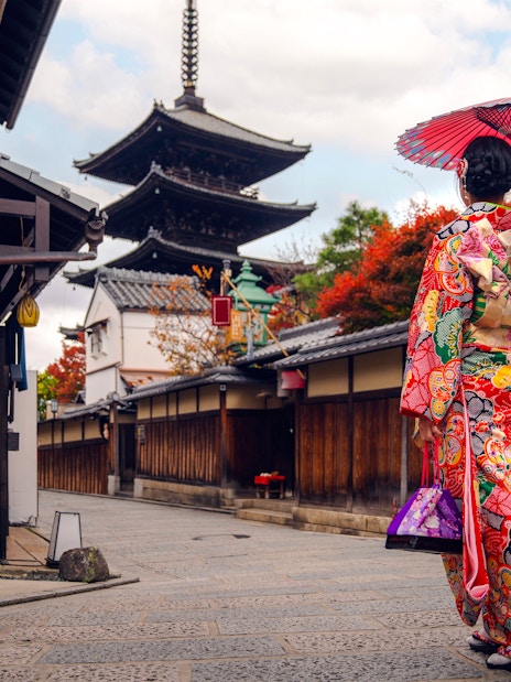 Asian woman in kimono walking near pagoda in Kyoto, Japan.