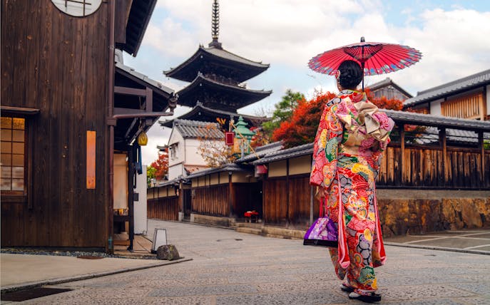 Asian woman in kimono walking near pagoda in Kyoto, Japan.