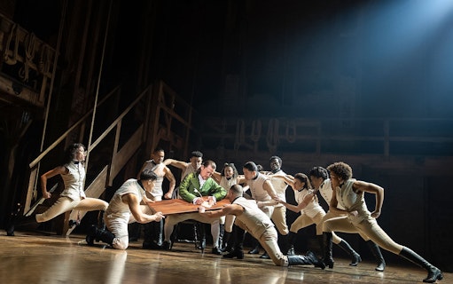 Cast performing a scene from the musical Hamilton on stage.