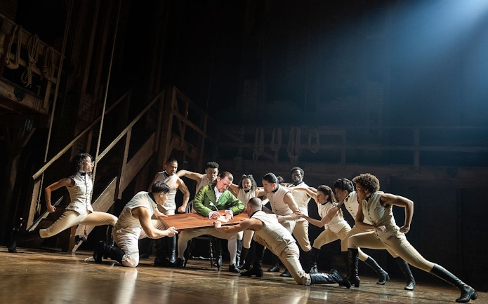 Cast performing a scene from the musical Hamilton on stage.