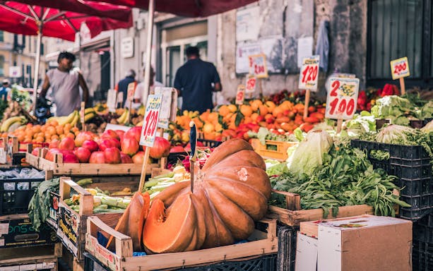 Market stall with fresh produce in the Decumani of Naples, featuring pumpkins and leafy greens.