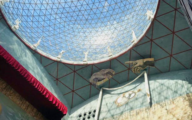 Interior view of glass dome in Dalí Museum, Spain, with artistic hand sculptures.