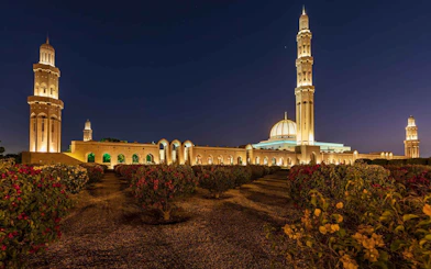 Sultan Qaboos Grand Mosque illuminated at night with gardens in Muscat, Oman.