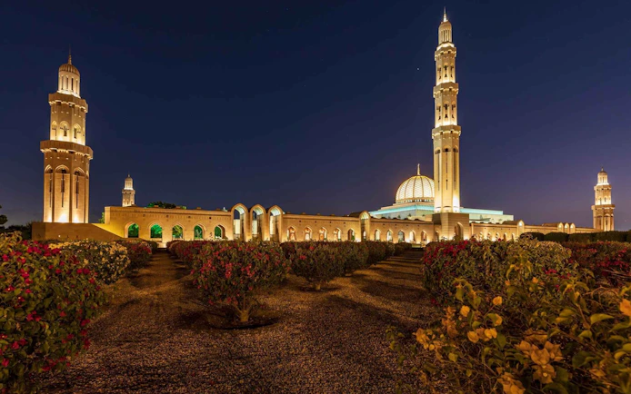 Sultan Qaboos Grand Mosque illuminated at night with gardens in Muscat, Oman.