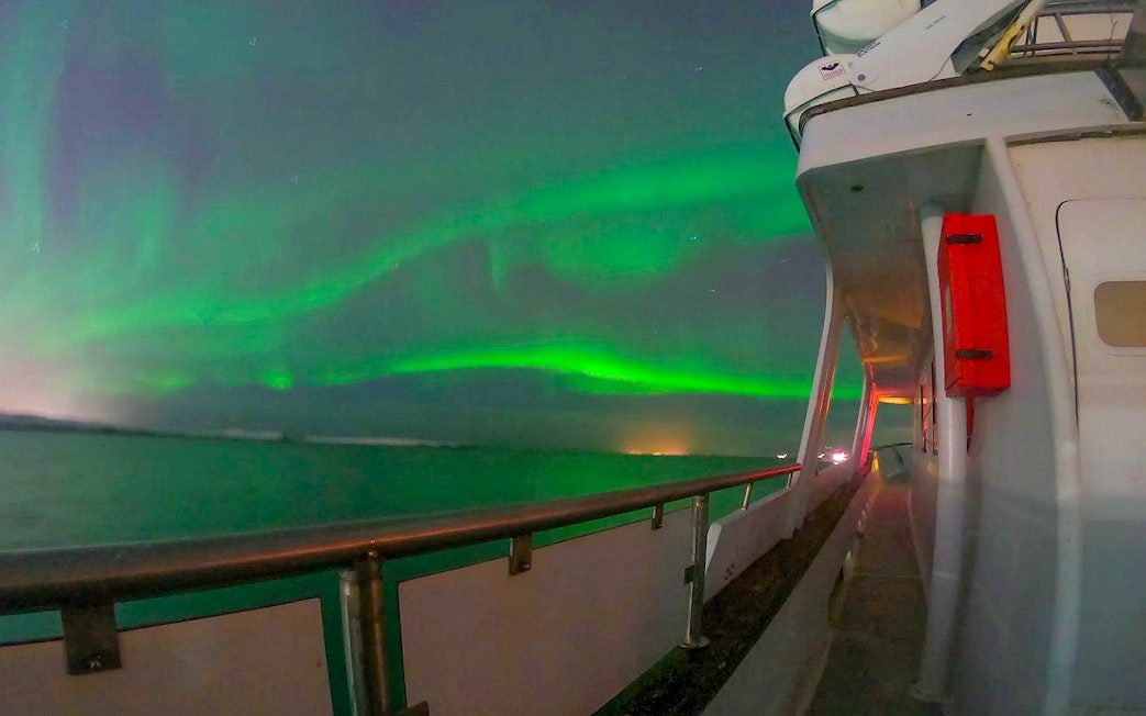 Northern lights over ocean from yacht deck during Northern Lights Yacht Cruise.