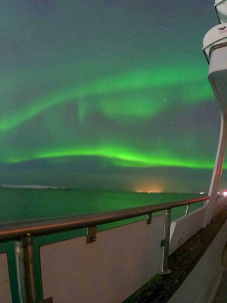 Northern lights over ocean from yacht deck during Northern Lights Yacht Cruise.