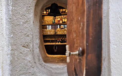View through a small door into a Florence artisan workshop with shelves of bottles and glasses.