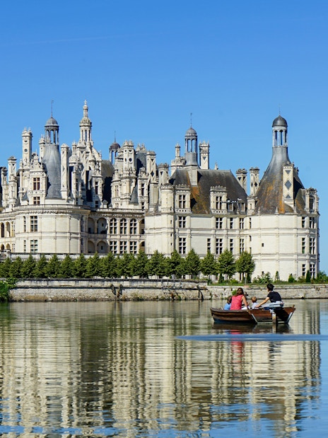 Chambord Castle with visitors in a boat on the surrounding moat, Loire Valley, France.