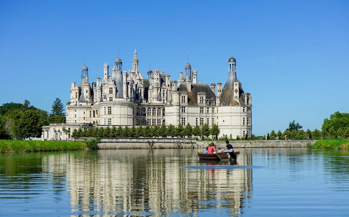 Chambord Castle with visitors in a boat on the surrounding moat, Loire Valley, France.