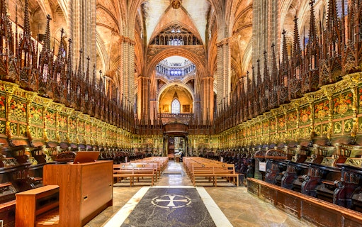 Interior of the Cathedral of Barcelona, featuring ornate choir stalls and vaulted ceilings.