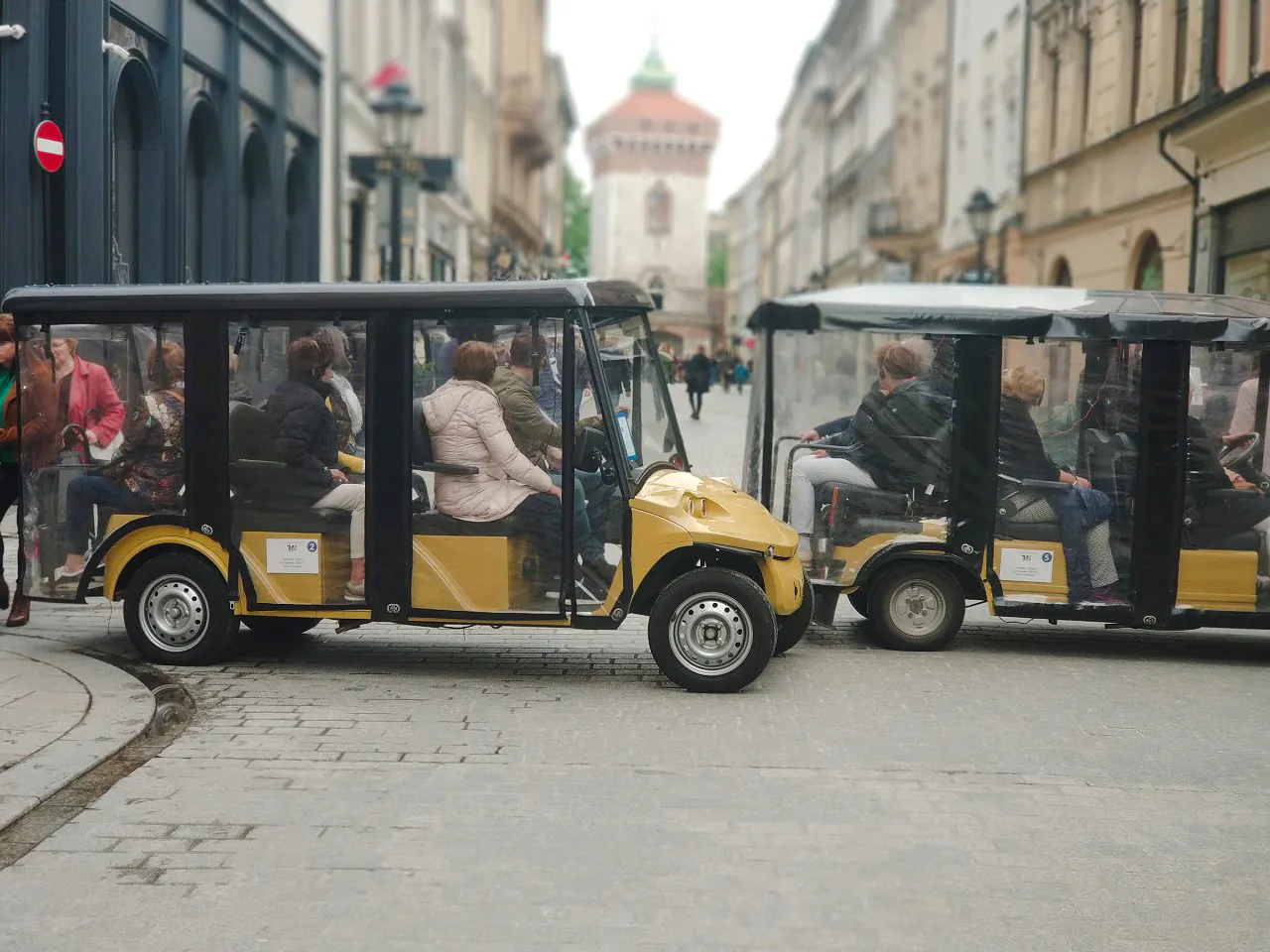 Golf carts with tourists in Krakow's Old Town near historic buildings.