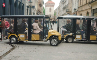 Golf carts with tourists in Krakow's Old Town near historic buildings.