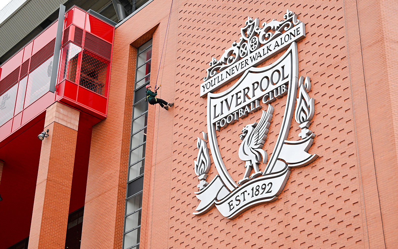 Abseiling down Anfield Stadium near Liverpool FC crest.