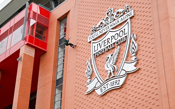 Abseiling down Anfield Stadium near Liverpool FC crest.