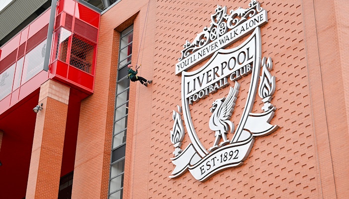 Abseiling down Anfield Stadium near Liverpool FC crest.