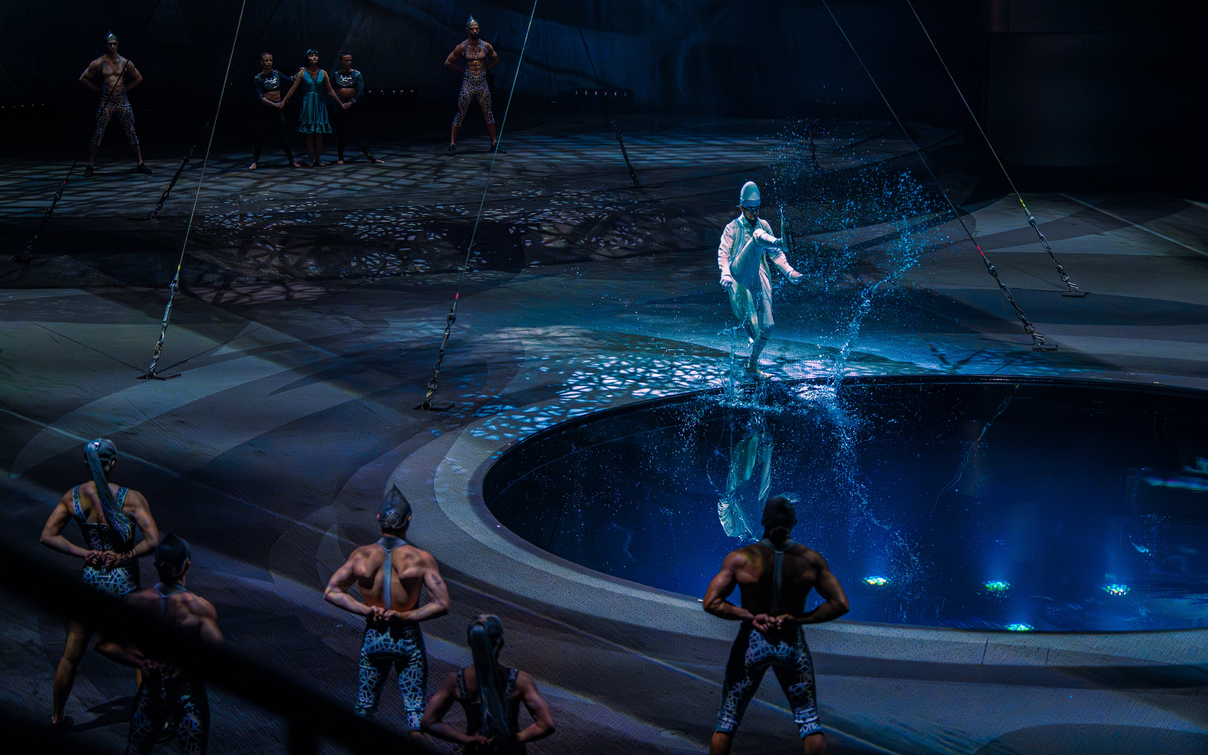 Performer splashing water during La Perle show in Dubai with acrobats in background.