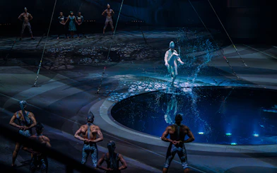 Performer splashing water during La Perle show in Dubai with acrobats in background.