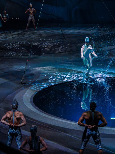 Performer splashing water during La Perle show in Dubai with acrobats in background.