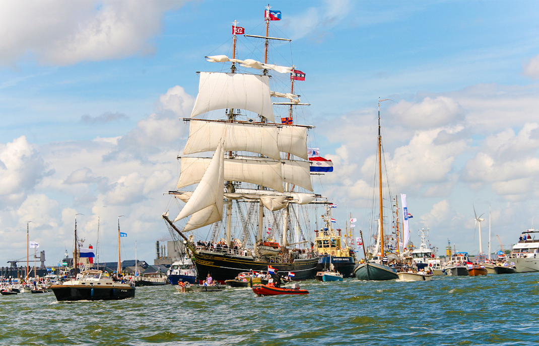 Tall ships sailing during SAIL Amsterdam event with flags and spectators.