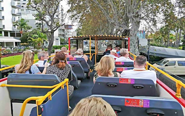 People seated on upper deck of City Sightseeing bus in Funchal, passing by trees and buildings.
