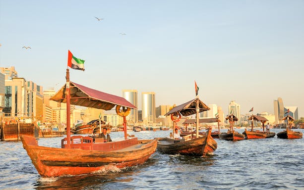 Traditional abras on Dubai Creek with city skyline in the background.