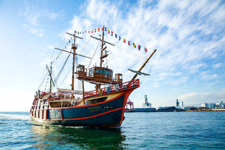 Santa Maria ship with colorful flags sailing in Osaka Bay, industrial port visible.