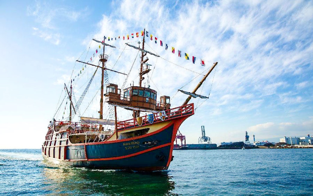 Santa Maria ship with colorful flags sailing in Osaka Bay, industrial port visible.