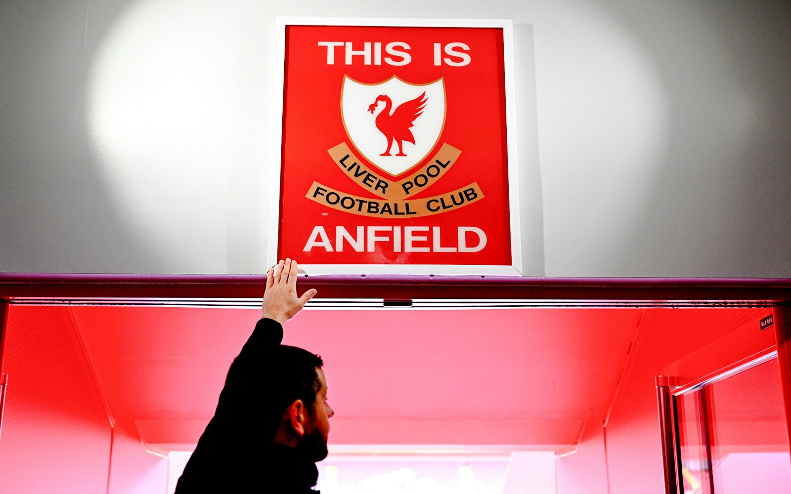 Hand touching "This is Anfield" sign at Liverpool FC's Anfield Stadium.
